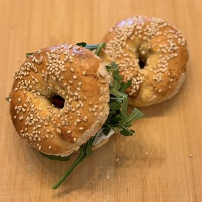 Zwei selbstgemachte Sesam-Bagels, einer mit Rucola belegt