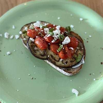 Brot mit gebratener Aubergine, Tomaten und Feta auf einem grünen Teller