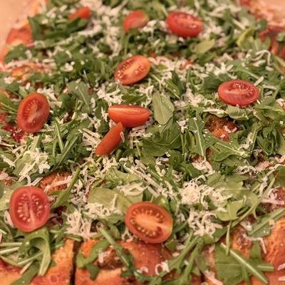 Pizza mit Rucola und Cocktailtomaten in Stücken