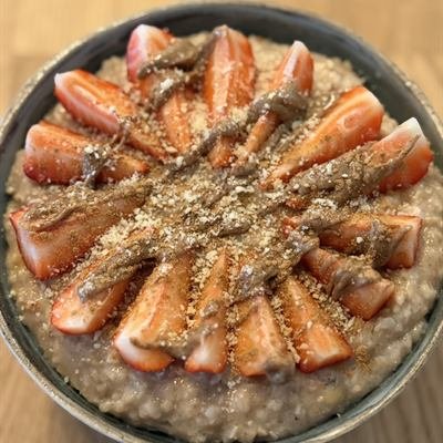 Porridge mit kreisförmig gelegten Erdbeeren, Mandelmus und gemahlenen Mandeln