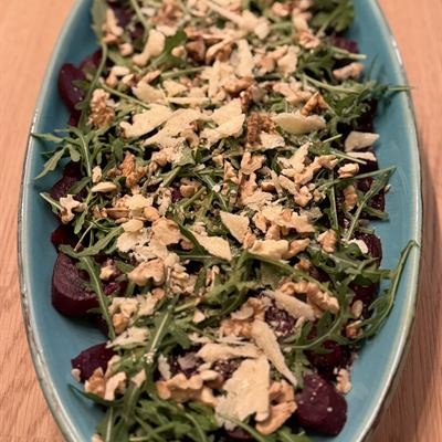 Dünne Rote-Bete-Scheiben mit Rucola, Walnüssen und Parmesan auf einer ovalen Platte