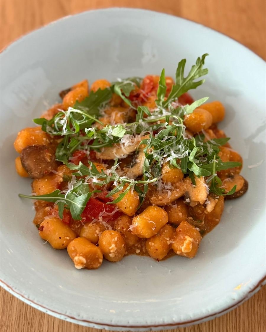 Gnocchi in Tomatensoße mit Champignons, Tomatenstücken, Rucola und geriebenem Parmesan auf einem hellblauen Teller